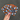 A hand with pink nail polish holds 3 Halloween-themed fabric cup sleeves. The sleeve is black and gray with a pattern of orange pumpkins, white ghosts, and stars, featuring a white label with  'the love mich collection' on it.